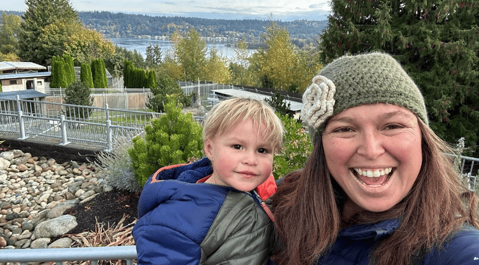 A mother in a green knit hat with a flower holds her blonde child in a green and blue jacket.