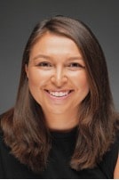 A headshot of a smiling white woman with shoulder-length brown hair.